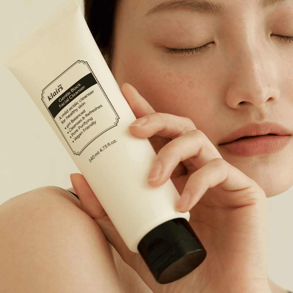 Henkilö pitää putkiloa Klairs Gentle Black Facial Cleanser poskeaan vasten, suljetut silmät ja luonnollinen ihonväri näkyvät taustalla.