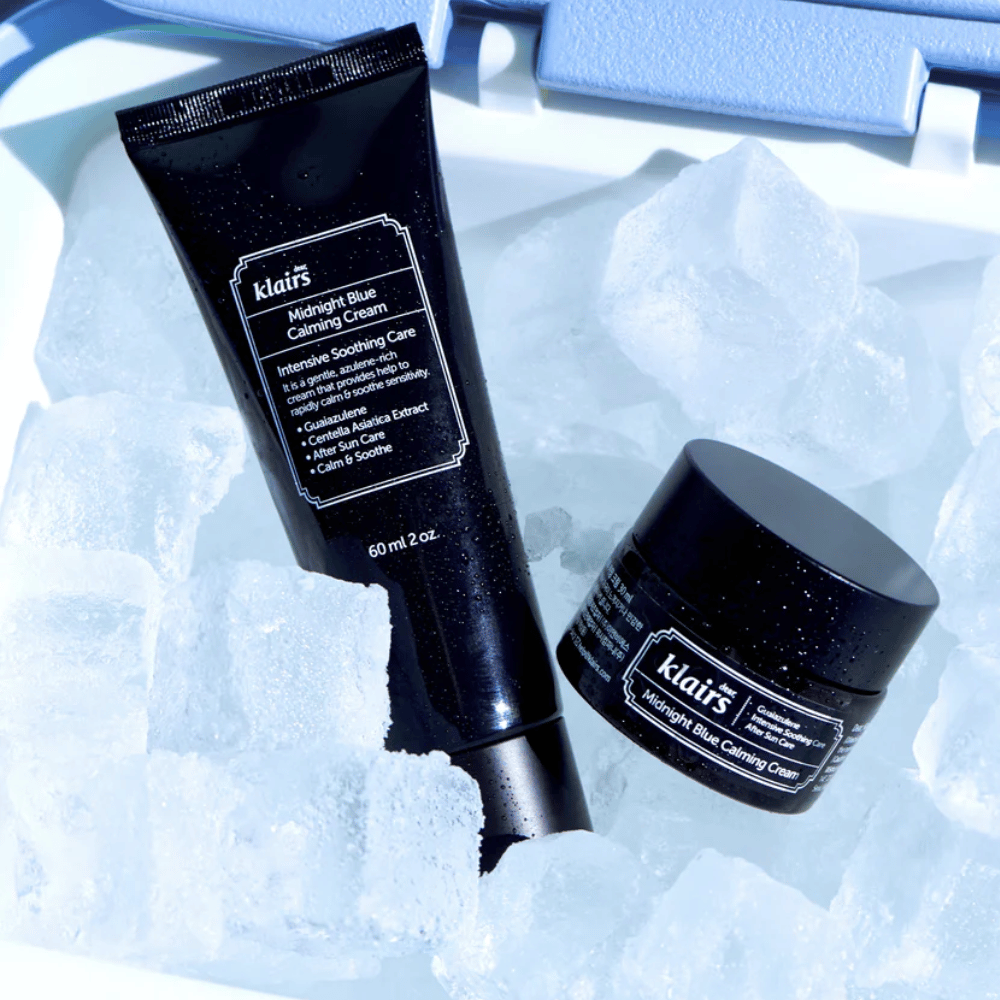 Tuubi ja purkki Klairs Midnight Blue Calming Cream ovat jääpalojen päällä, keskittyen rauhoittaviin ja kosteuttaviin ominaisuuksiin, sinisellä taustalla.