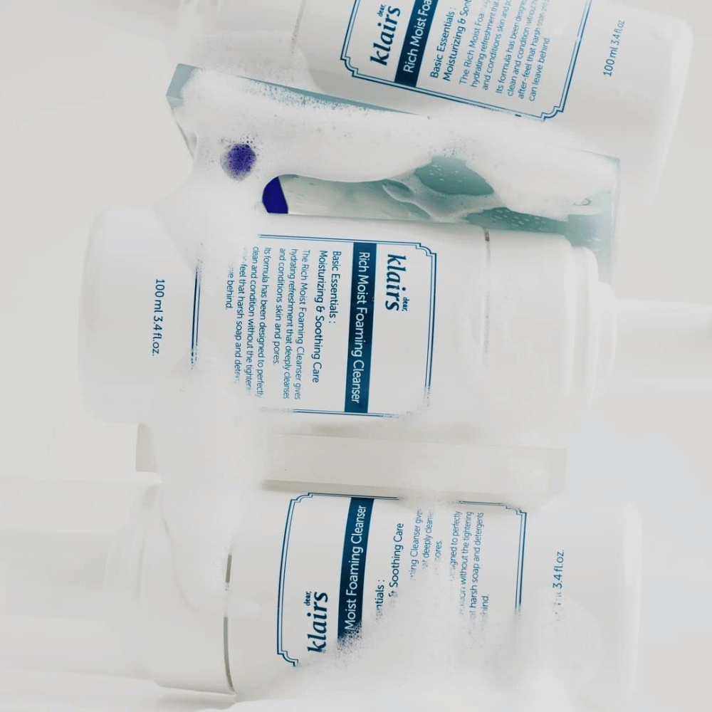 Kolme Klairs Rich Moist Foaming Cleanser pulloa, jotka on peitetty vaahdolla ja vesipisaroilla, asetettuna valkoiselle pinnalle.