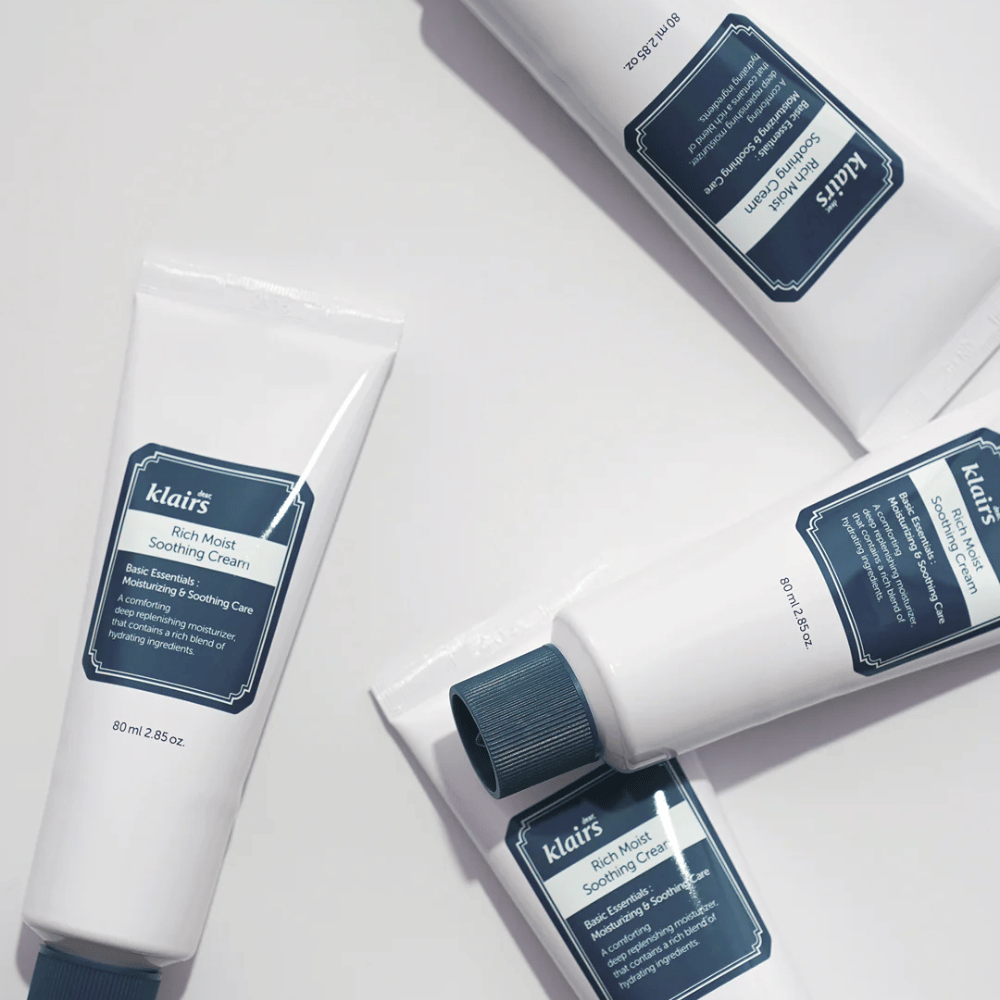 Useita putkia Klairs Rich Moist Soothing Cream strategisesti sijoitettu vaalealle pinnalle, varjojen luodessa syvyyttä.