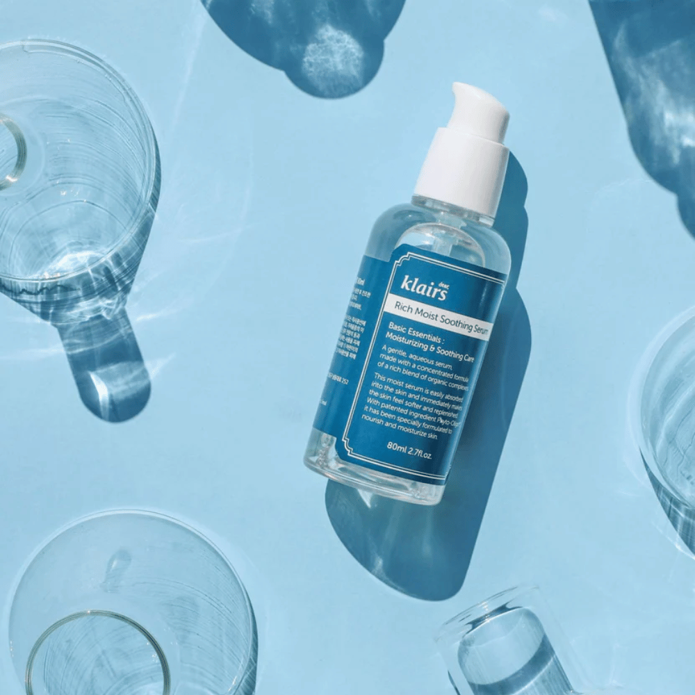 Pullo Klairs Rich Moist Soothing Serum vesilasien joukossa heijastuksilla sinisellä taustalla.
