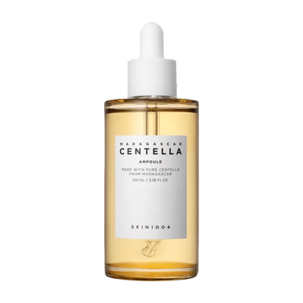 Kuva esittää pullon "Madagascar Centella Asiatica 100 Ampoule" SKIN1004. Pullo sisältää 100 ml ja väittää olevansa valmistettu puhtaasta Madagaskarin centellasta. Tuote näyttää olevan ihonhoitoseerumi, ja yksinkertainen etiketti antaa vaikutelman puhtaudesta ja luonnollisuudesta. Tippakorkilla varustettu pullo ehdottaa, että tämä on huolellisesti annosteltu ihonhoitotuote.