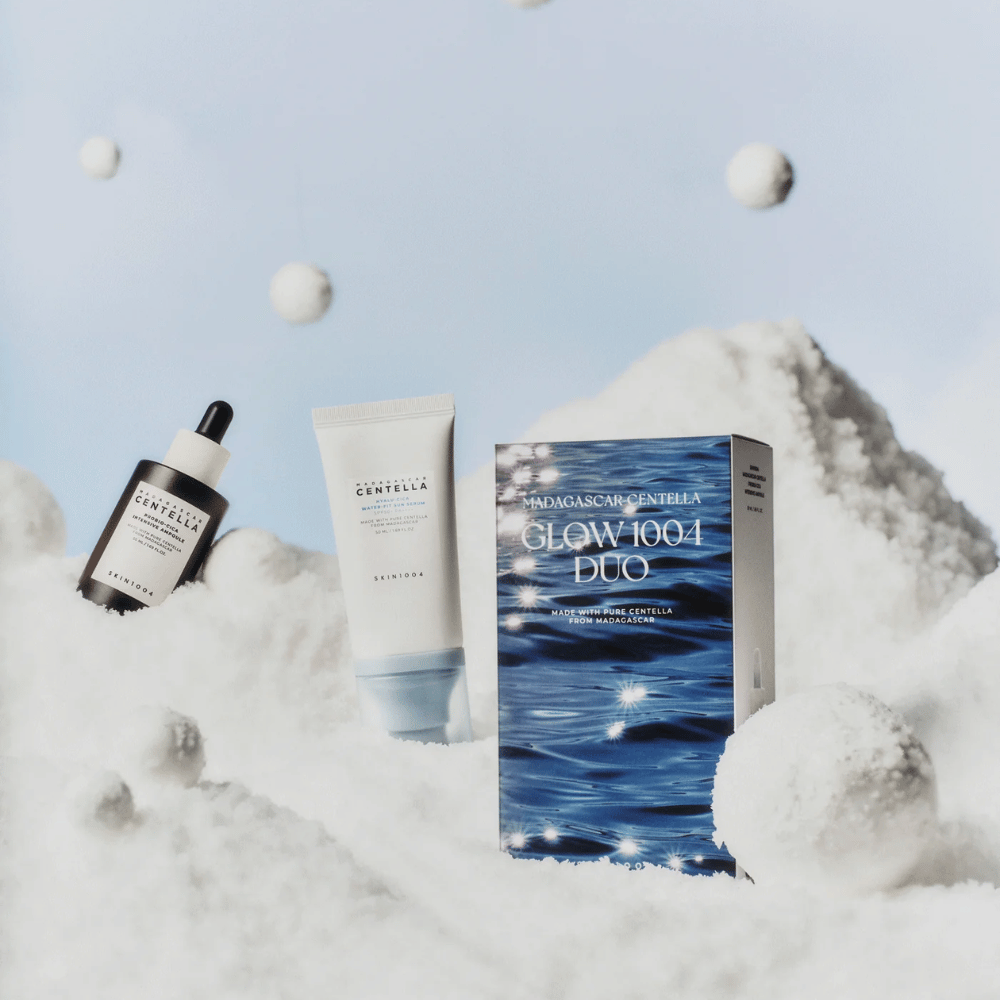 Kuva näyttää ihonhoitosetin "Madagascar Centella Glow 1004 Duo" SKIN1004, asetettuna taustalle, joka esittää lunta ja taivasta.