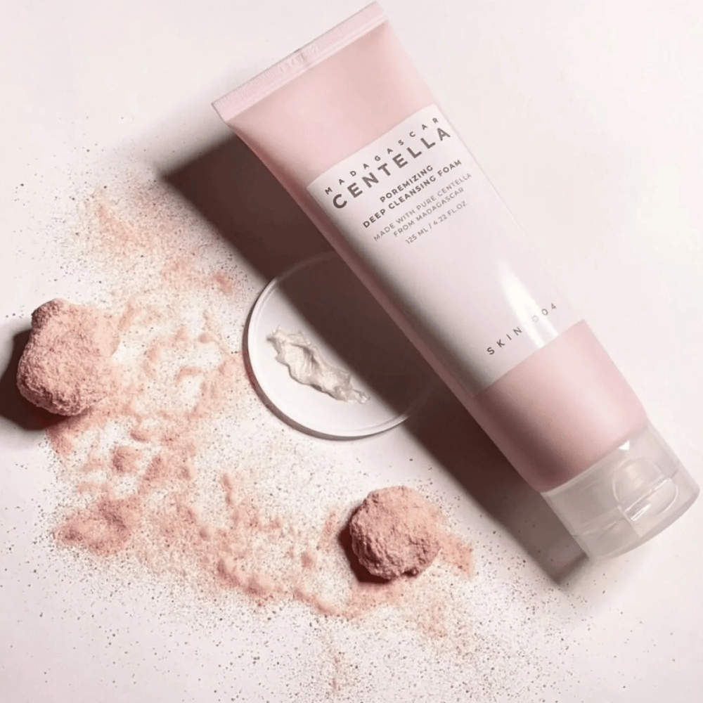 Madagascar Centella Poremizing Deep Cleansing Foam on esitelty vaaleanpunaisessa tuubissa. Tuubi on vaalealla alustalla yhdessä vaaleanpunaisen jauheen kanssa, joka antaa puhtauden ja raikkauden tunteen. Tuote on suunniteltu syväpuhdistamaan ihoa puhtaan Madagaskarin centellan avulla.