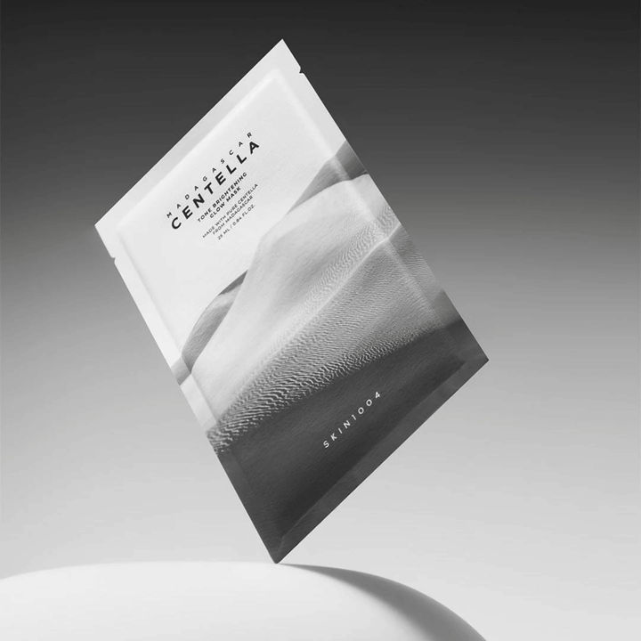 Sheet mask-pakkaus merkiltä SKIN1004 leijumassa harmaata taustaa vasten minimalistisella muotoilulla.