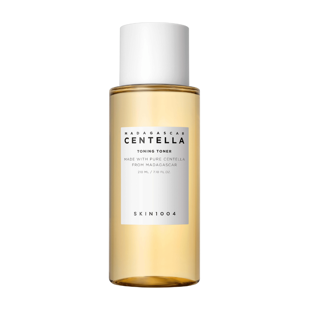 Kuva näyttää pullon ihonhoitotuotetta, merkitty "Madagascar Centella Toning Toner" SKIN1004. Tuotteen ilmoitetaan sisältävän 210 ml tai 7.10 fl.oz ja se on valmistettu puhtaasta Madagaskarin centellasta. Pakkaus on yksinkertainen ja tyylikäs, läpinäkyvä pullo ja kultainen sävyinen neste sisällä, mikä luo ylellisyyden ja puhtauden tunteen. Tuotemerkin logo SKIN1004 on selvästi näkyvissä etiketin alaosassa.