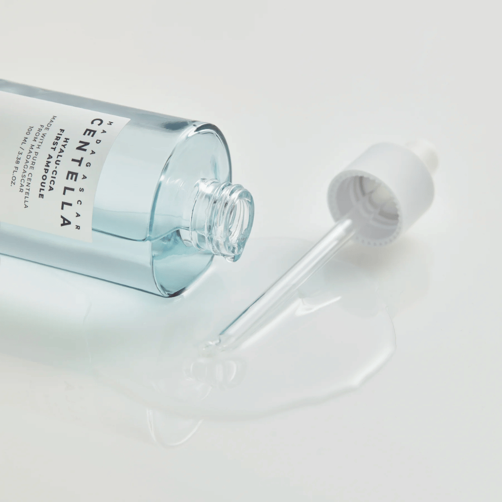 Lähikuva avoimesta pullosta Skin1004 Madagascar Centella Hyalu-Cica First Ampoule pipetillä, joka makaa ja seerumi leviää valkoisella pinnalla.