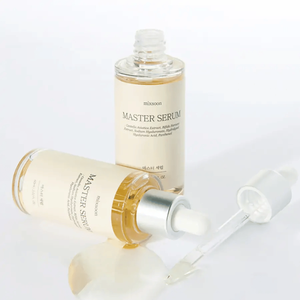 Kaksi pulloa Mixsoon Master Serum, yksi pystyasennossa ja toinen makuuasennossa avoimen pipetin kanssa, jossa seerumi on valunut valkoiselle pinnalle.