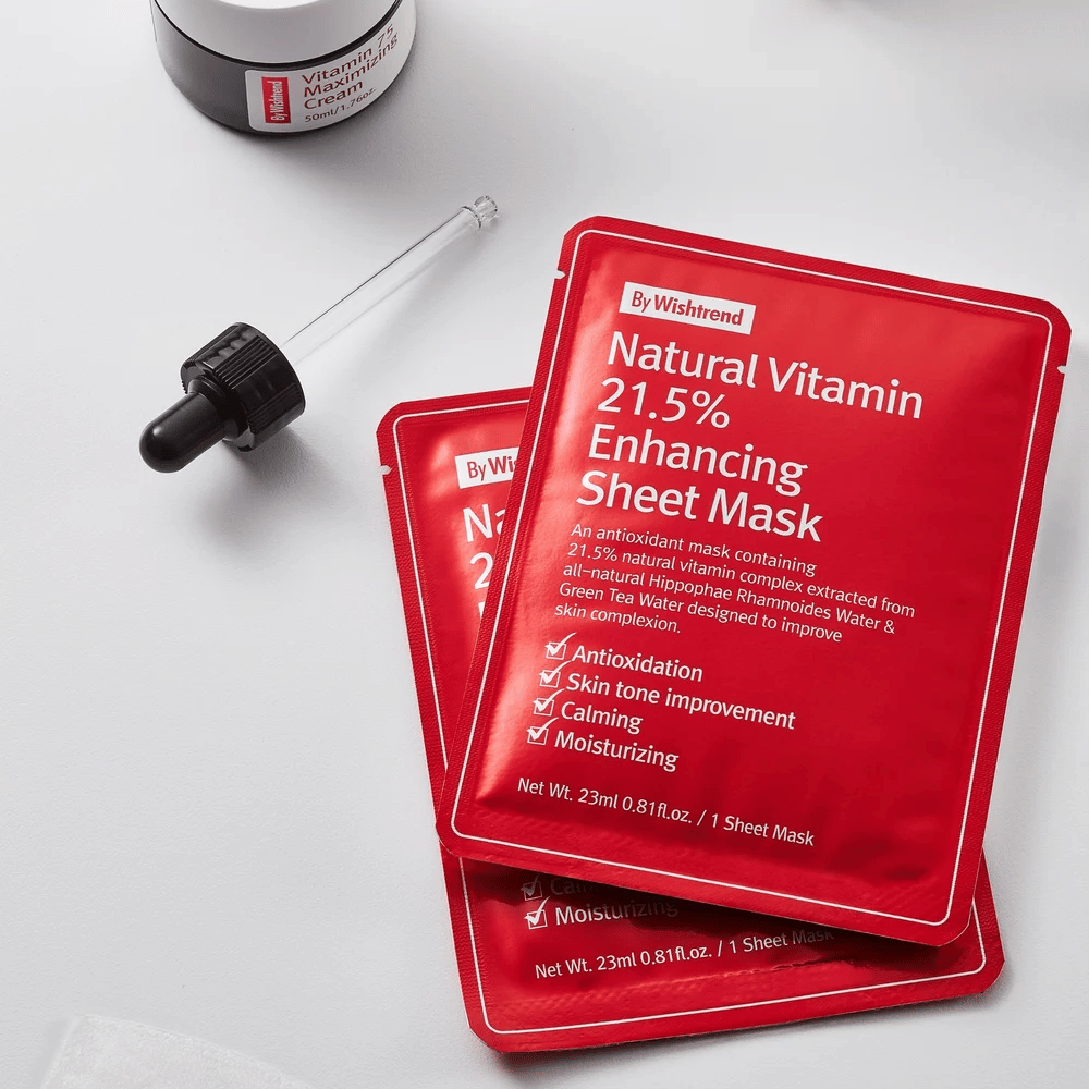 By Wishtrend Natural Vitamin 21.5% Enhancing Sheet mask punaisissa pakkauksissa, asetettu valkoiselle pinnalle pipetin ja kasvovoidepurkin kanssa.