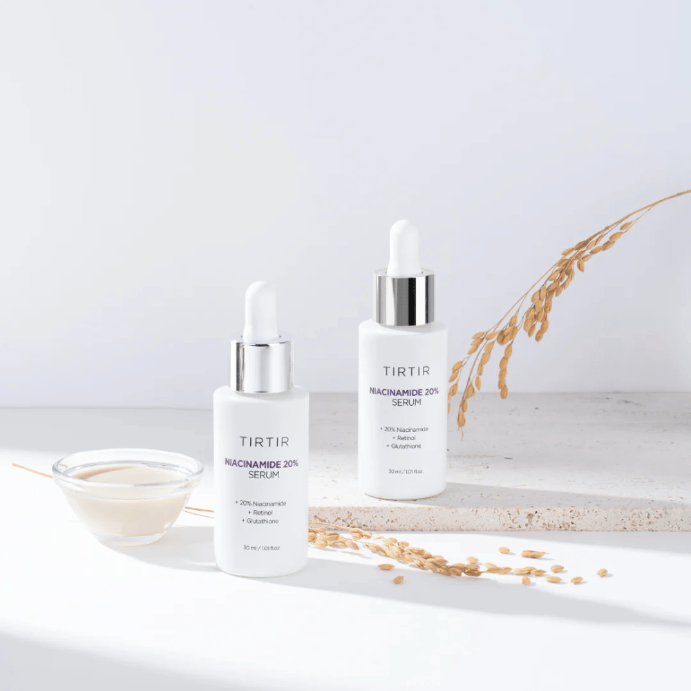 Kaksi Tirtirs "Niacinamide 20% Serum" -pulloa on esillä vaalealla pinnalla pienen kulhon kanssa, jossa on kermainen aine, ja muutama kuiva kasvinoksa. Seerumi sisältää 20 % niasiiniamidia, retinolia ja glutationia, mikä auttaa parantamaan ihon ulkonäköä ja rakennetta.