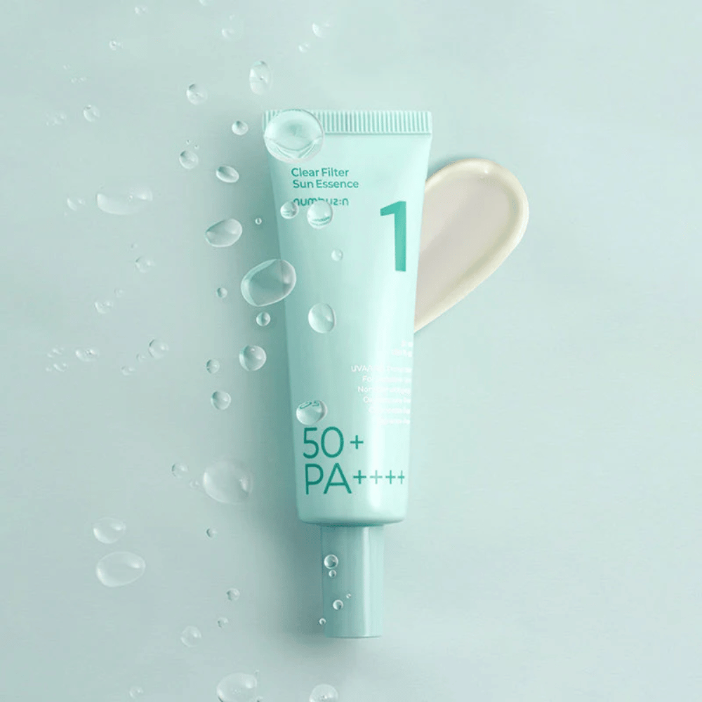 Vaaleansininen tuubi, jossa on No.1 Clear Filter Sun Essence SPF 50+ PA++++. Tuubi on koristeltu vesipisaroilla ja tuotteen näyte näkyy vieressä. Tuote on suunniteltu tarjoamaan korkea aurinkosuojakerroin ja suoja UVA/UVB-säteiltä.