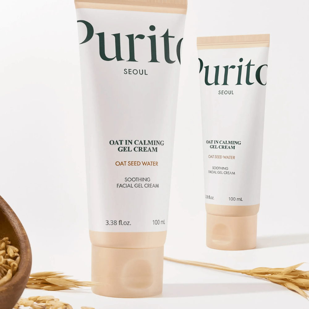 Purito Oat-In Calming Gel Cream beigessä tuubissa, sijoitettuna kauranjyvien kanssa. Rauhoittaa herkkää ihoa kauravedellä ja kevyellä geelitekstuurilla.