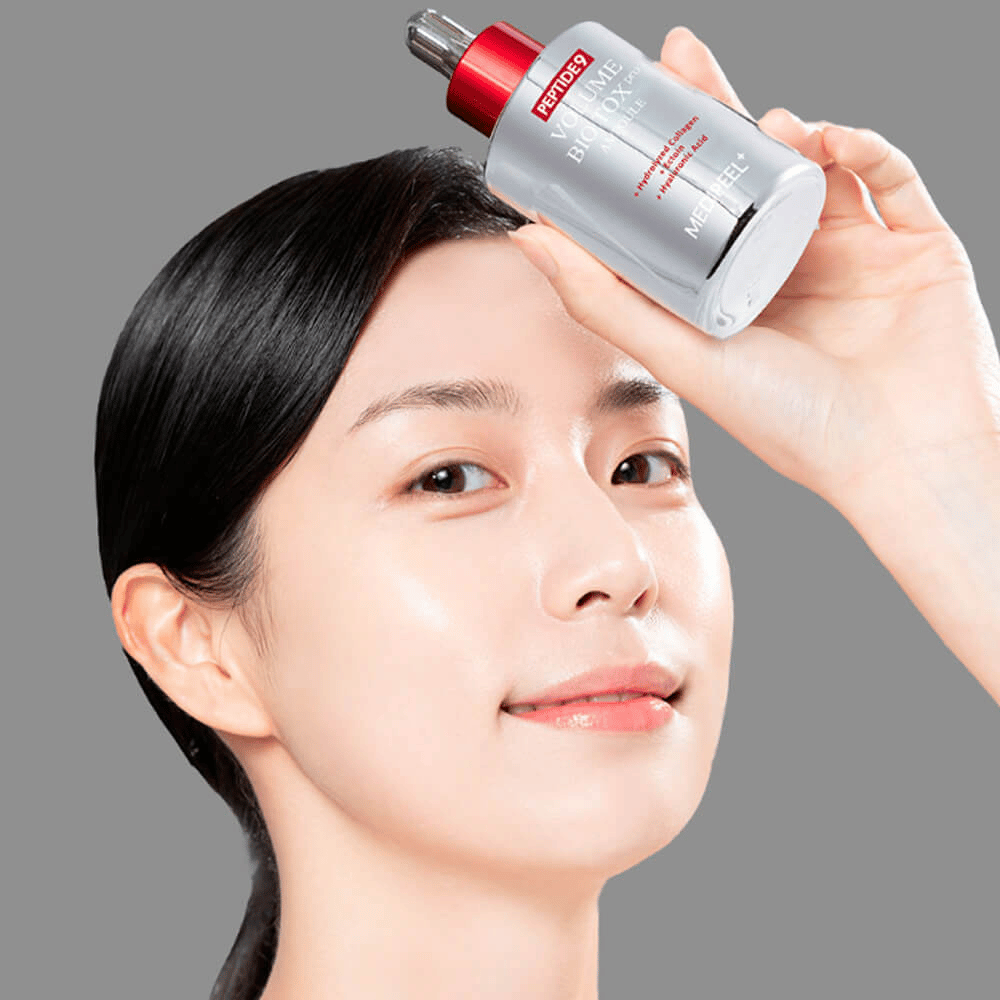Henkilö pitää MEDI-PEEL Peptide 9 Volume Bio Tox Pro Ampoule -ampullia otsaa vasten. Iho näyttää kosteutetulta ja säteilevältä – seerumi vahvistaa kimmoisuutta ja kiinteyttä.