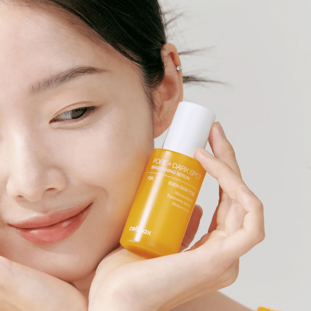 Malli pitää Celimax Pore + Dark Spot Brightening Serum lähellä kasvoja, näyttää säteilevän ihon.