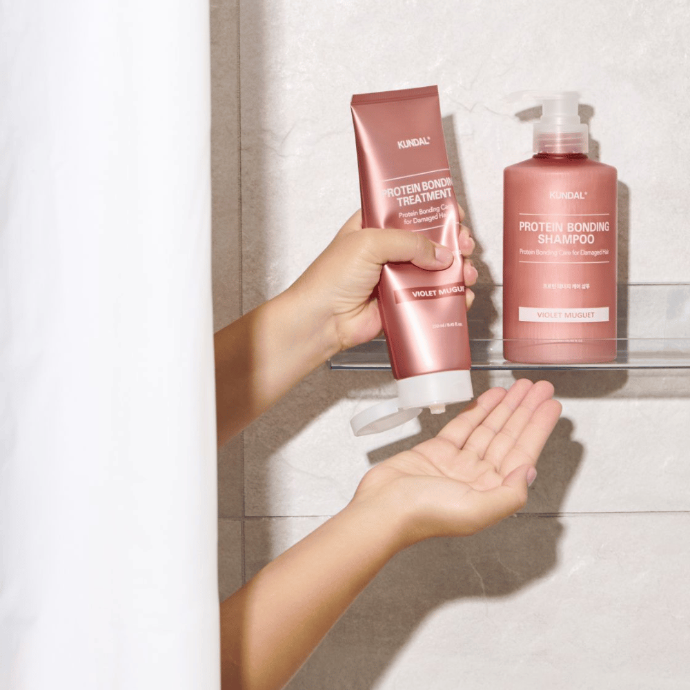KUNDAL Protein Bonding Treatment Violet Muguet används i duschen, med Protein Bonding Shampoo placerad på hyllan bredvid.