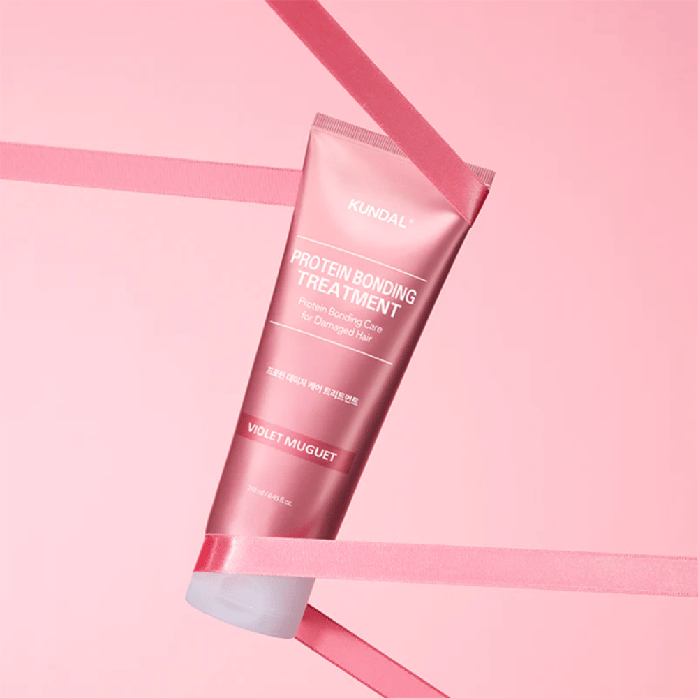 KUNDAL Protein Bonding Treatment Violet Muguet vaaleanpunaisessa tuubissa 250 ml vaaleanpunaista taustaa vasten koristeellisilla nauhoilla.