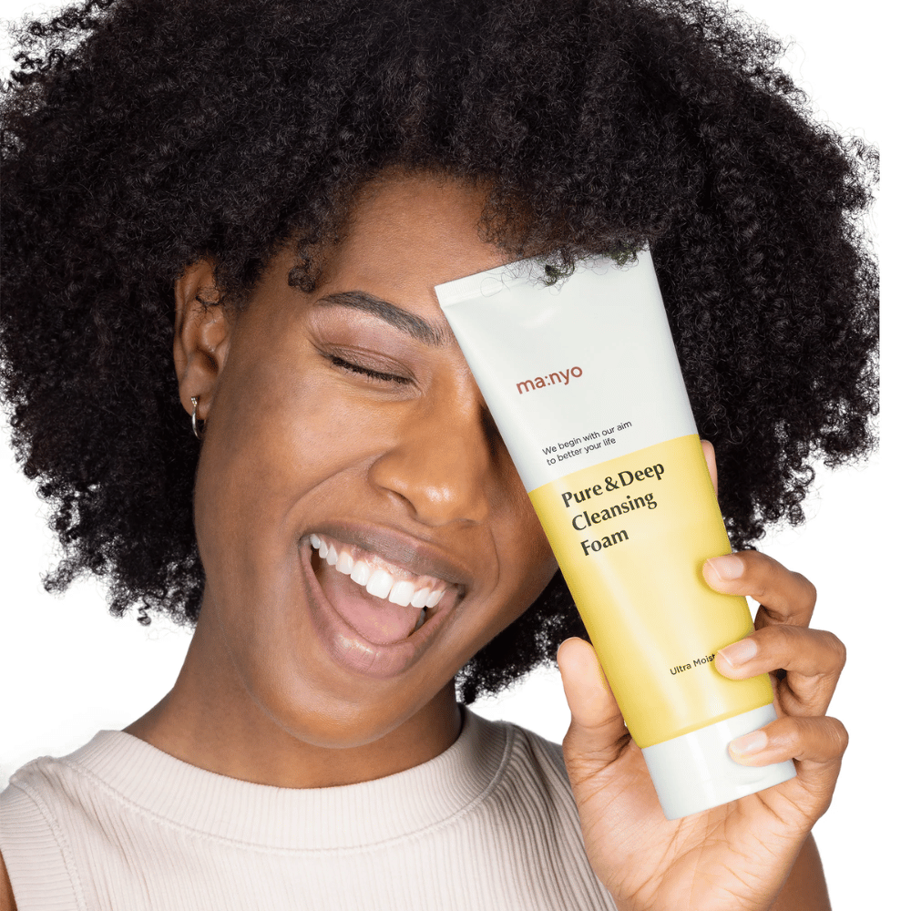 Nainen, jolla on kiharat hiukset, pitää Ma:nyo Pure & Deep Cleansing Foam – hellävarainen korealainen puhdistusaine, joka poistaa tehokkaasti lian ja meikin kuivattamatta ihoa.