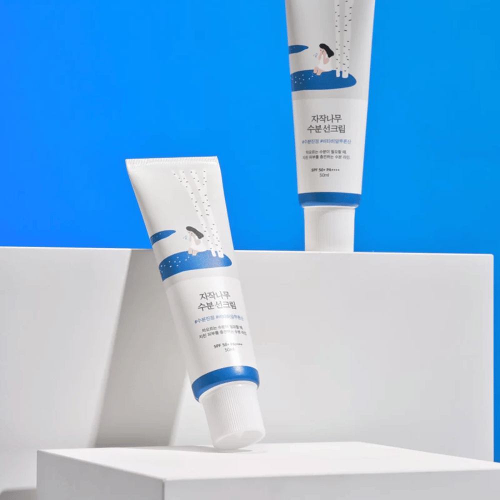 Kaksi tuubia Round Lab Birch Juice Moisturizing Sunscreen SPF50+ PA++++ 50ml, jotka sijaitsevat sinisellä taustalla.
