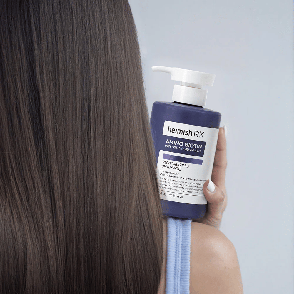 Heimish RX Amino Biotin Revitalizing Shampoo pidetään kädessä pitkien, kiiltävien hiusten edessä – näyttää intensiivisen ravitsemuksen ja kosteutuksen tuloksen kuiville hiuksille.