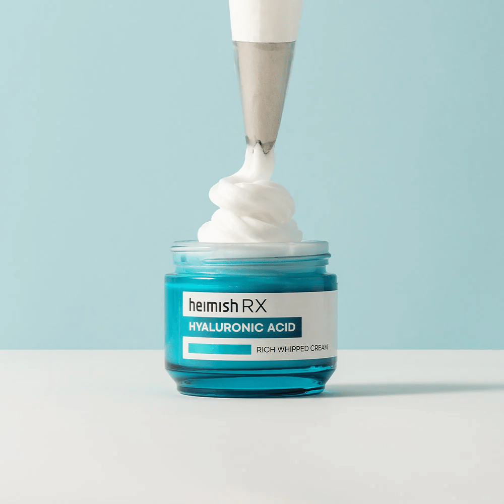 Heimish RX Hyaluronic Acid Rich Whipped Cream sinisessä lasipurkissa, jossa pursotinpussi levittää kuohkean voiteen. Kosteuttava kasvovoide, joka sisältää hyaluronihappoa intensiiviseen kosteutukseen ja pehmeälle, täyteläiselle iholle.