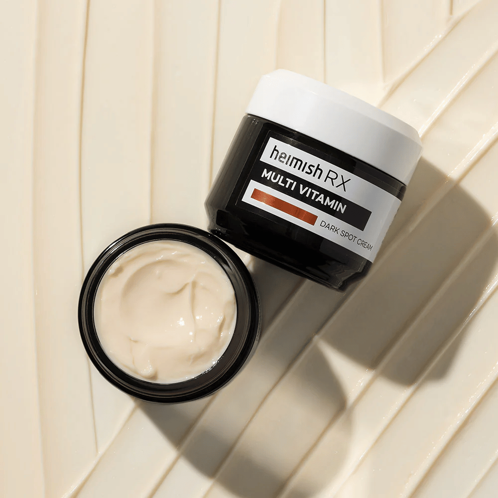 heimish RX Multi Vitamin Dark Spot Cream – ravitseva kasvovoide tummien läiskien vähentämiseen ja ihon tasaisemman sävyn saavuttamiseksi. Voiteen sileä koostumus näkyy avoimessa purkissa, jossa on elegantti pakkaus.