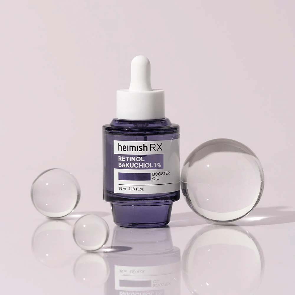 Heimish RX Retinol Bakuchiol Booster Oil 1% tyylikkäässä violetissa lasipullossa pipetillä. Öljy on asetettu heijastavalle pinnalle lasikuulien ympäröimänä, mikä luo ylellisen ja modernin tunnelman.