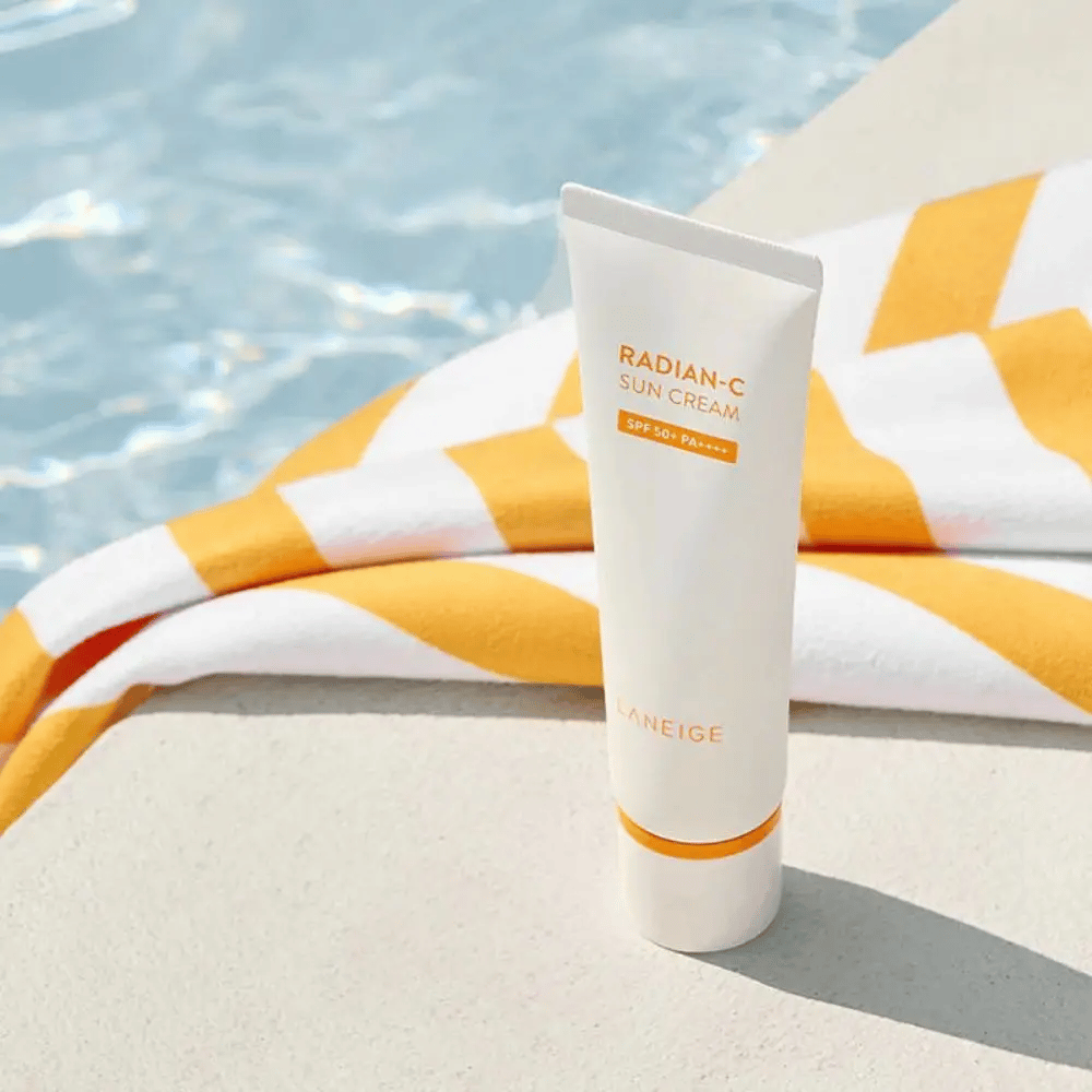 LANEIGE Radian-C Sun Cream seisoo uima-altaan reunalla kelta-valkoraitaisen pyyhkeen kanssa taustalla.