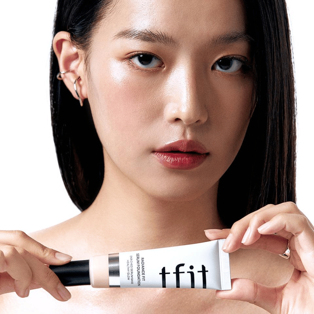 Malli, jolla on kiiltävä, sileä iho, pitelee TFIT Radiance Fit Serum Foundation, mikä korostaa tuotteen luonnollista viimeistelyä ja hehkua.