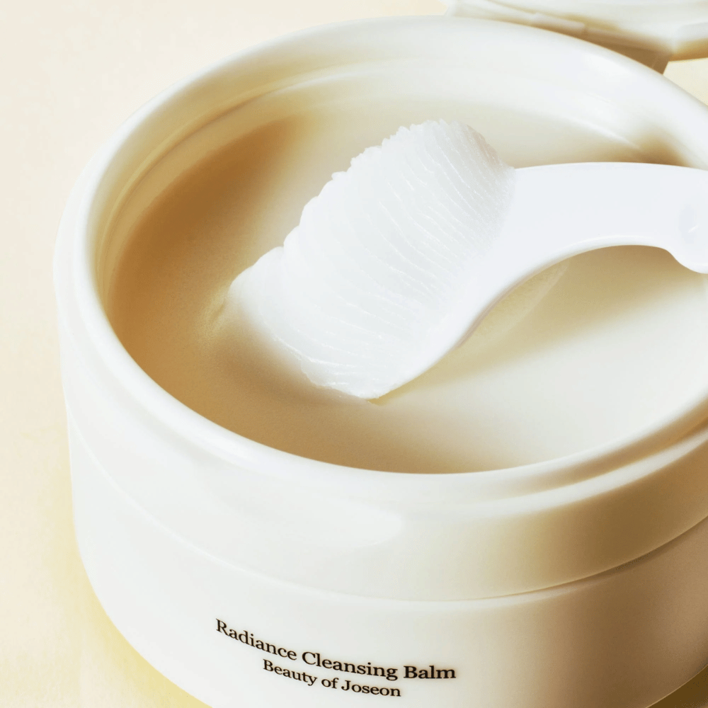 Lähikuva Beauty of Joseon Radiance Cleansing Balm purkissa lastan kanssa – silkkinen balm, joka puhdistaa ja kosteuttaa.