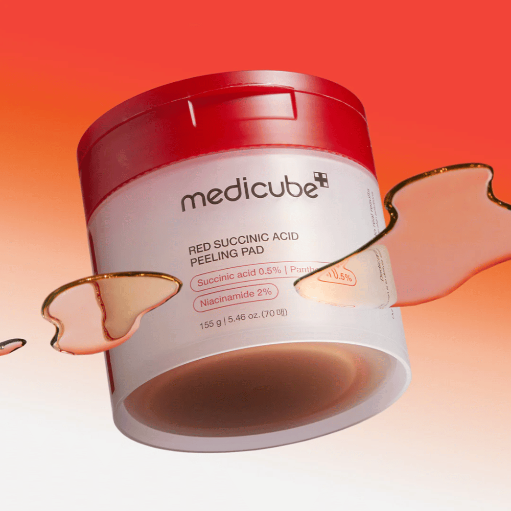 Medicube Red Succinic Acid Peeling Pad valkoisessa ja punaisessa purkissa, sijoitettuna punaoranssia liukuvärjättyä taustaa vasten. Tuote sisältää meripihkahappoa ja niasiiniamidia kuorintaan ja ihon parantamiseen. Nestemäinen koostumus näkyy purkin ympärillä.