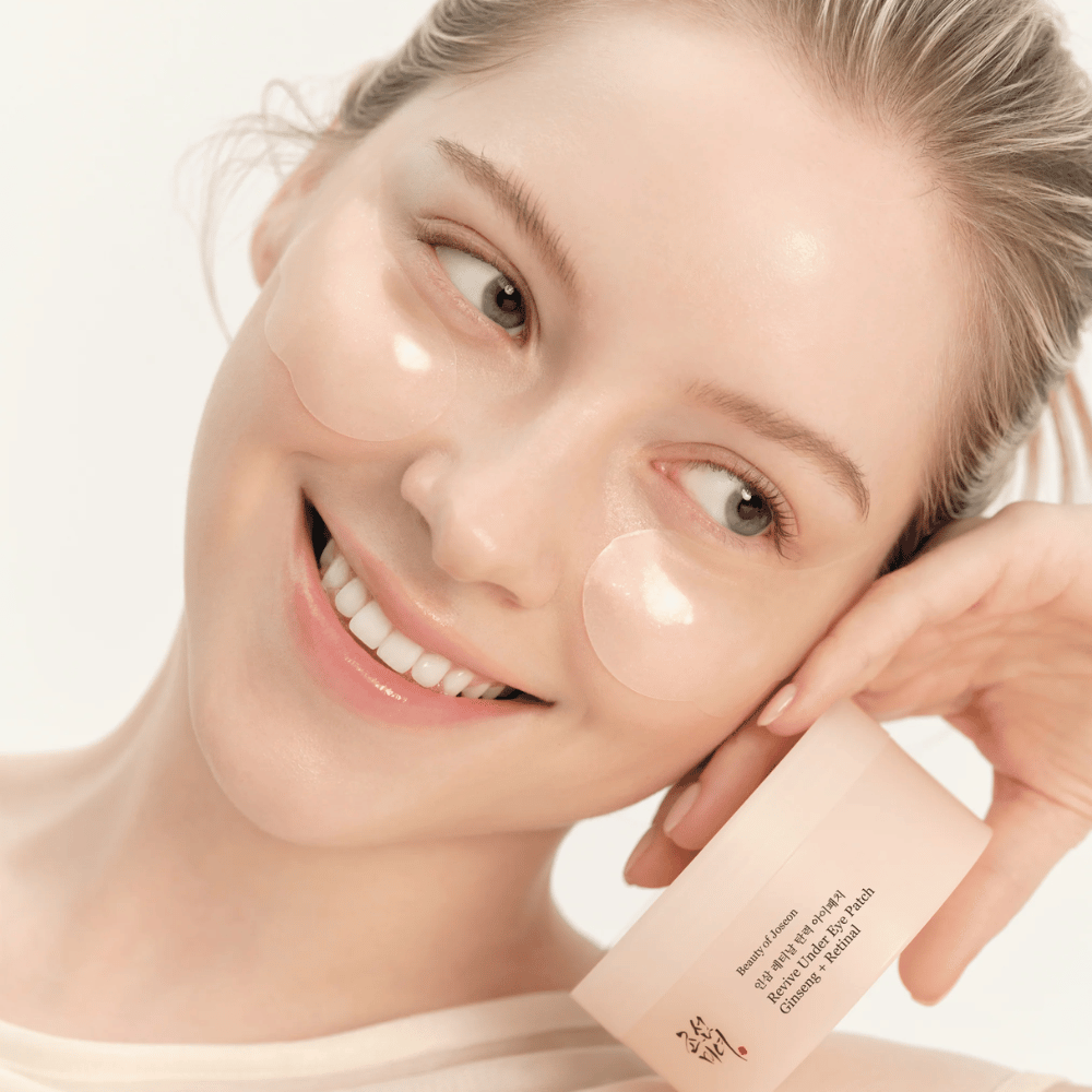 Malli, jolla on Beauty of Joseon silmänympäryslaput ja tuote kädessä, silmänympäryslaput ginsengillä ja retinalilla virkeämmän ja sileämmän silmänympärysalueen saamiseksi.