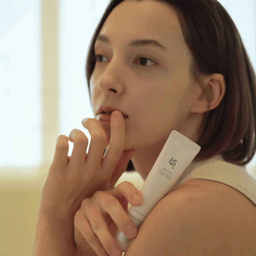 Malli pitää kädessään Beauty of Joseon Revive Eye Serum ja levittää varovasti iholle kosteutetun ja sileän silmänympärysihon saavuttamiseksi.