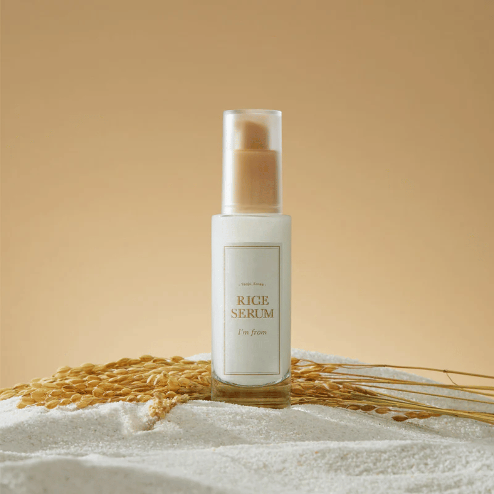 Pullo "I'm from" Rice Serum, ympäröitynä riisinjyvillä ja riisin tähkillä lämpimää taustaa vasten.