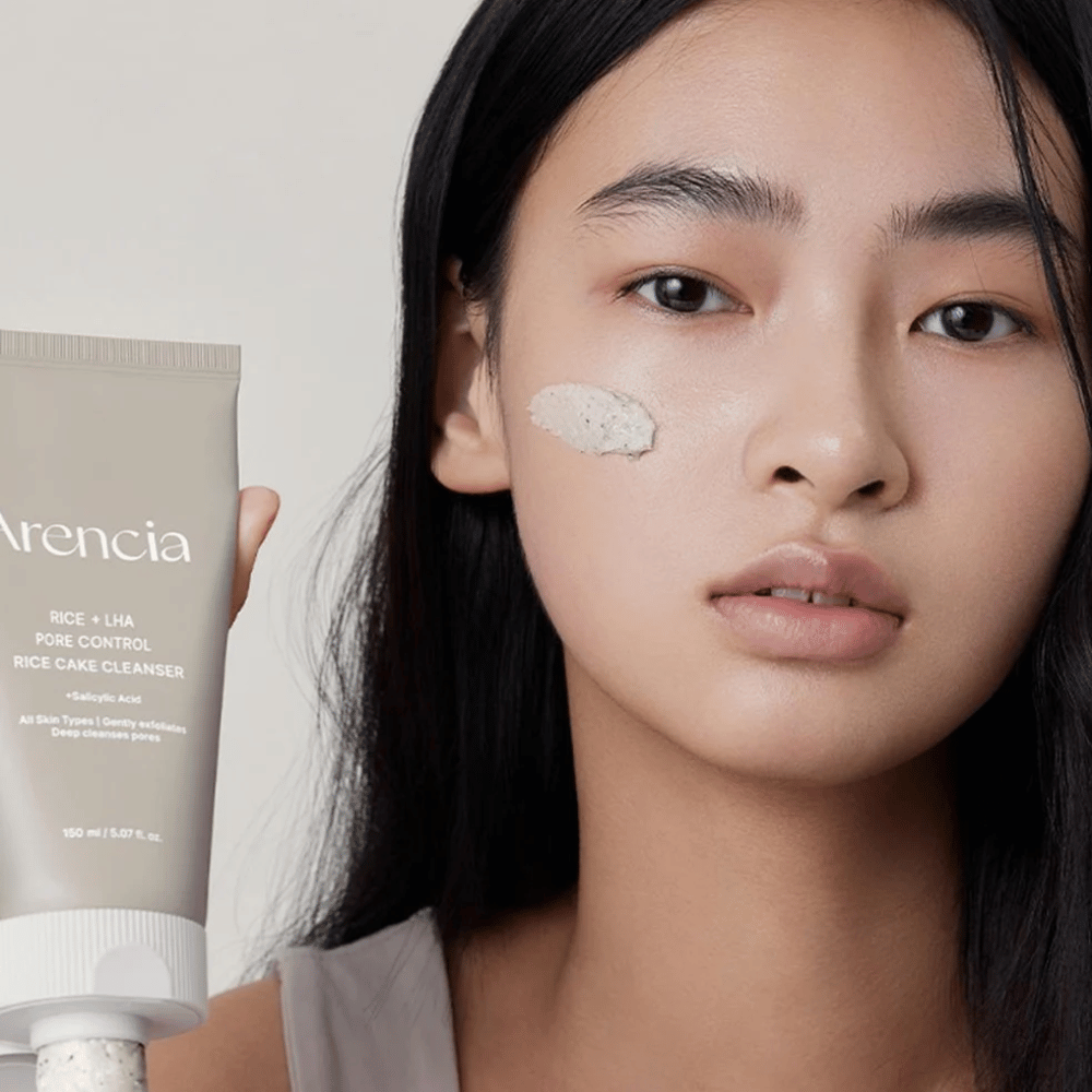 Malli, joka pitelee Arencia Rice + LHA Pore Control Rice Cake Cleanser poskelle levitettynä, havainnollistaa mietoa mutta tehokasta huokospuhdistusta päivittäiseen käyttöön.