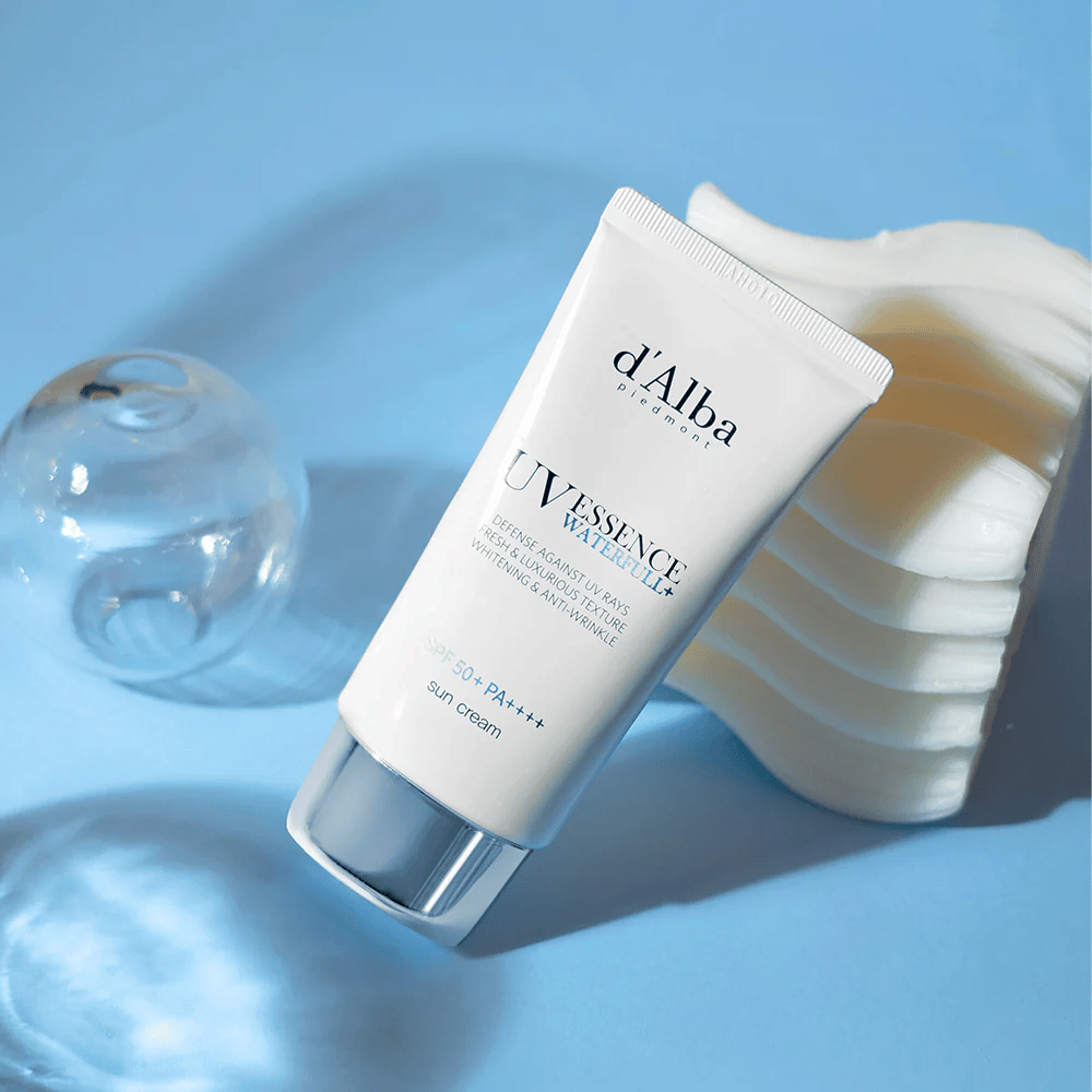 d'Alba UV Essence Waterfull+ Sun Cream -aurinkovoide suojakertoimella SPF 50+ PA++++, sijoitettuna siniselle taustalle valonheijastuksilla ja koriste-elementeillä – korostaa aurinkovoiteen raikkaita ja kosteuttavia ominaisuuksia.