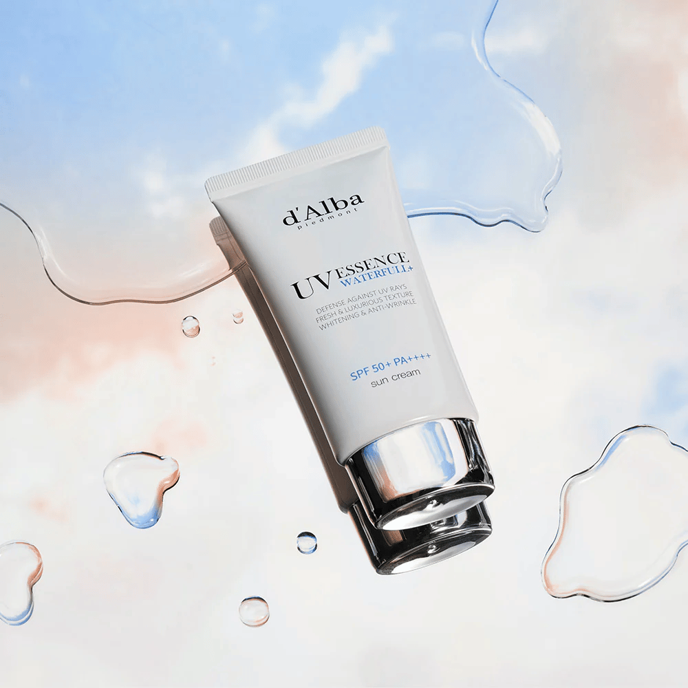 Tuotekuva d'Alba UV Essence Waterfull+ Sun Cream -aurinkovoiteesta, jonka suojakerroin on SPF 50+ PA++++, sijoitettuna taustalle, jossa on vesiroiskeita ja sinipunainen taivas – symboloi kevyttä ja kosteuttavaa aurinkosuojaa.