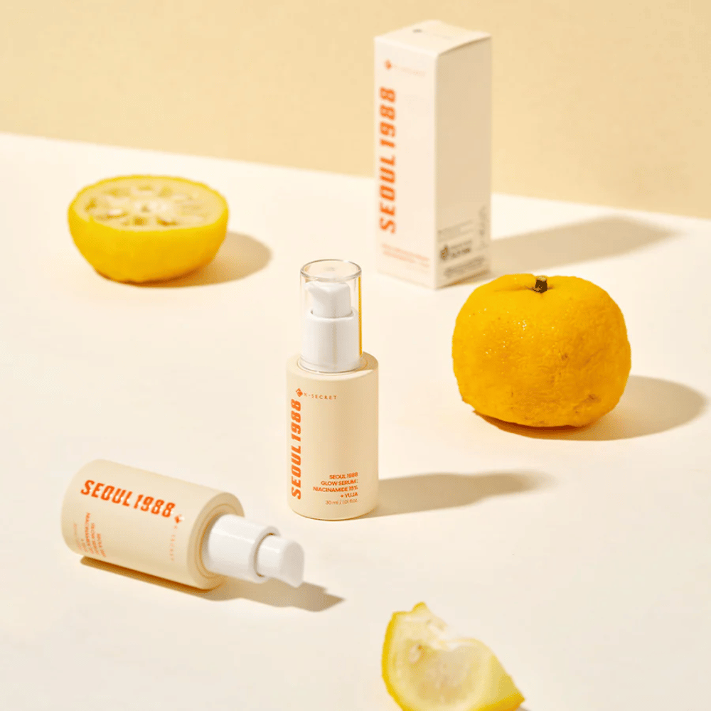 Useita pulloja ja pakkauksia Seoul 1988 Glow Serum järjestettynä kokonaisina ja puolikkaina yuja-hedelminä taustalla.
