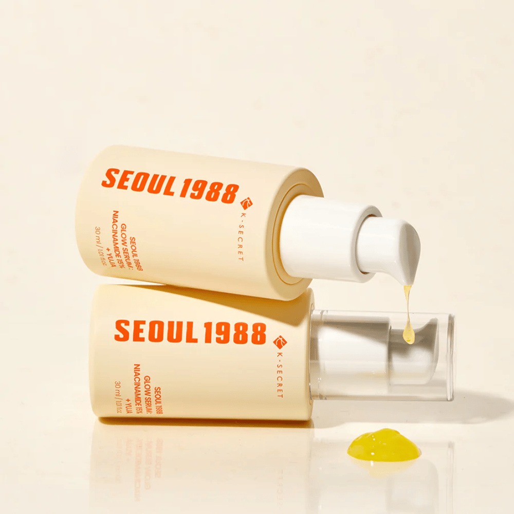 Kaksi pulloa Seoul 1988 Glow Serum makuuasennossa ja pystyasennossa, keltaista seerumia tippumassa pumpusta.