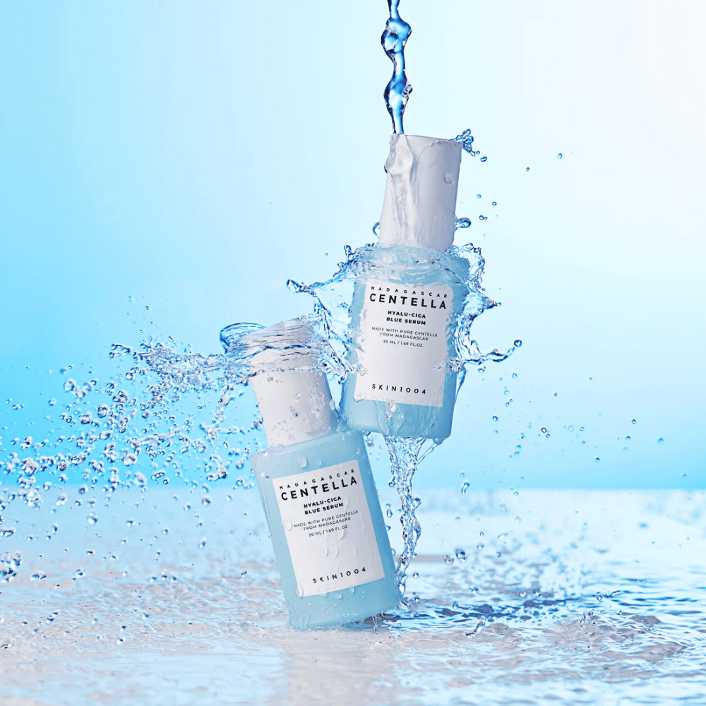 Kaksi pulloa SKIN1004 Madagascar Centella Hyalu-Cica Blue Serum osuu veden kaskadiin vaaleansinisellä taustalla.
