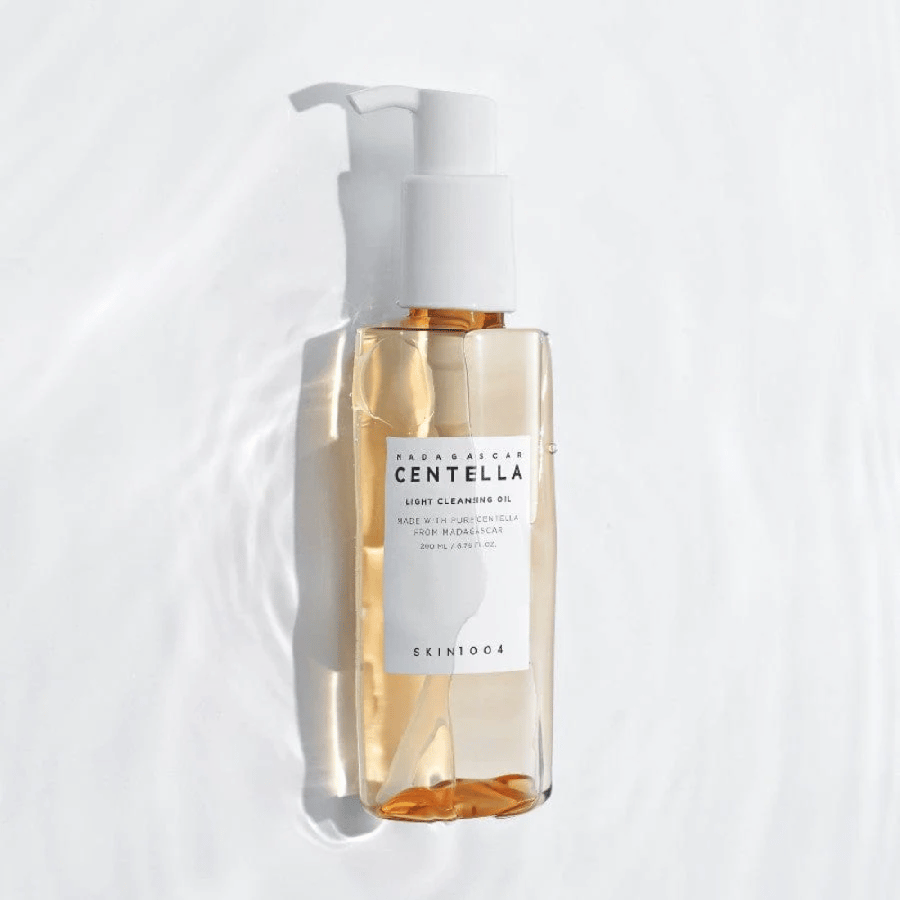 SKIN1004 Madagascar Centella Light Cleansing Oil valkoisella taustalla pehmeillä vesiheijastuksilla, jotka korostavat läpinäkyvää pulloa ja kultaista sisältöä.