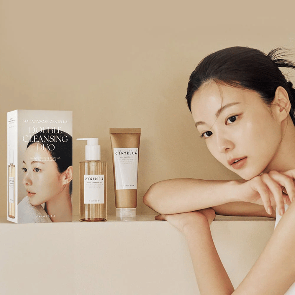 SKIN1004 Madagascar Centella Double Cleansing Duo Set pakkauksen kanssa, öljypohjainen puhdistus, vaahtopuhdistus ja malli kosteutetulla iholla beigeä taustaa vasten.
