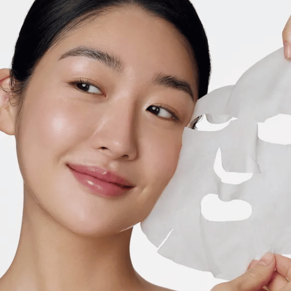 Kuva esittää henkilöä, joka käyttää kasvonaamiota, erityisesti "Retinol Intense Daily Mask" Some By Mi. Naamio on suunniteltu päivittäiseen käyttöön ja sisältää retinolia ihon tekstuurin parantamiseksi, hienojen juonteiden vähentämiseksi ja tasaisemman ihonsävyn saavuttamiseksi.