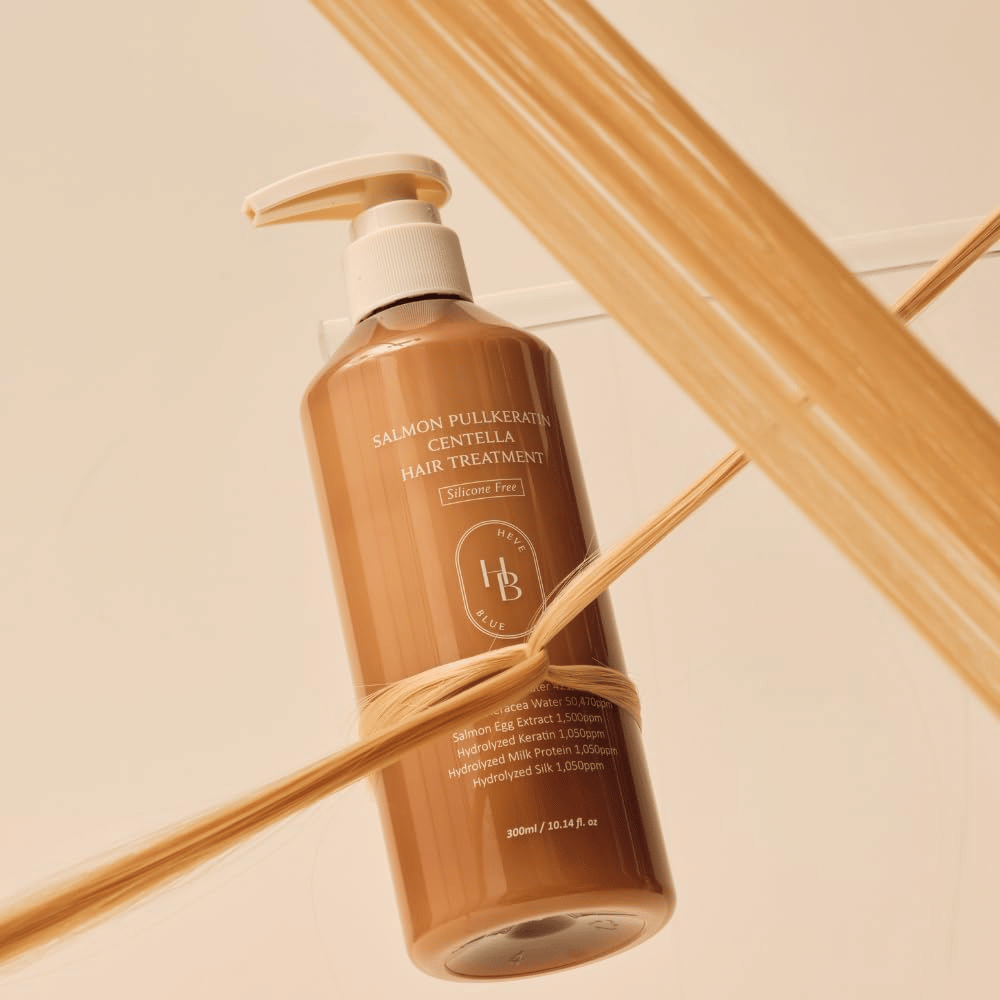 Heveblue Salmon Pullkeratin Centella Hair Treatment ruskeassa pullossa hiussuortuvien ympäröimänä. Kuva tuo esiin hiushoidon hoitavat ominaisuudet keskittyen kiiltoon, vahvuuteen ja silkinpehmeisiin hiuksiin.