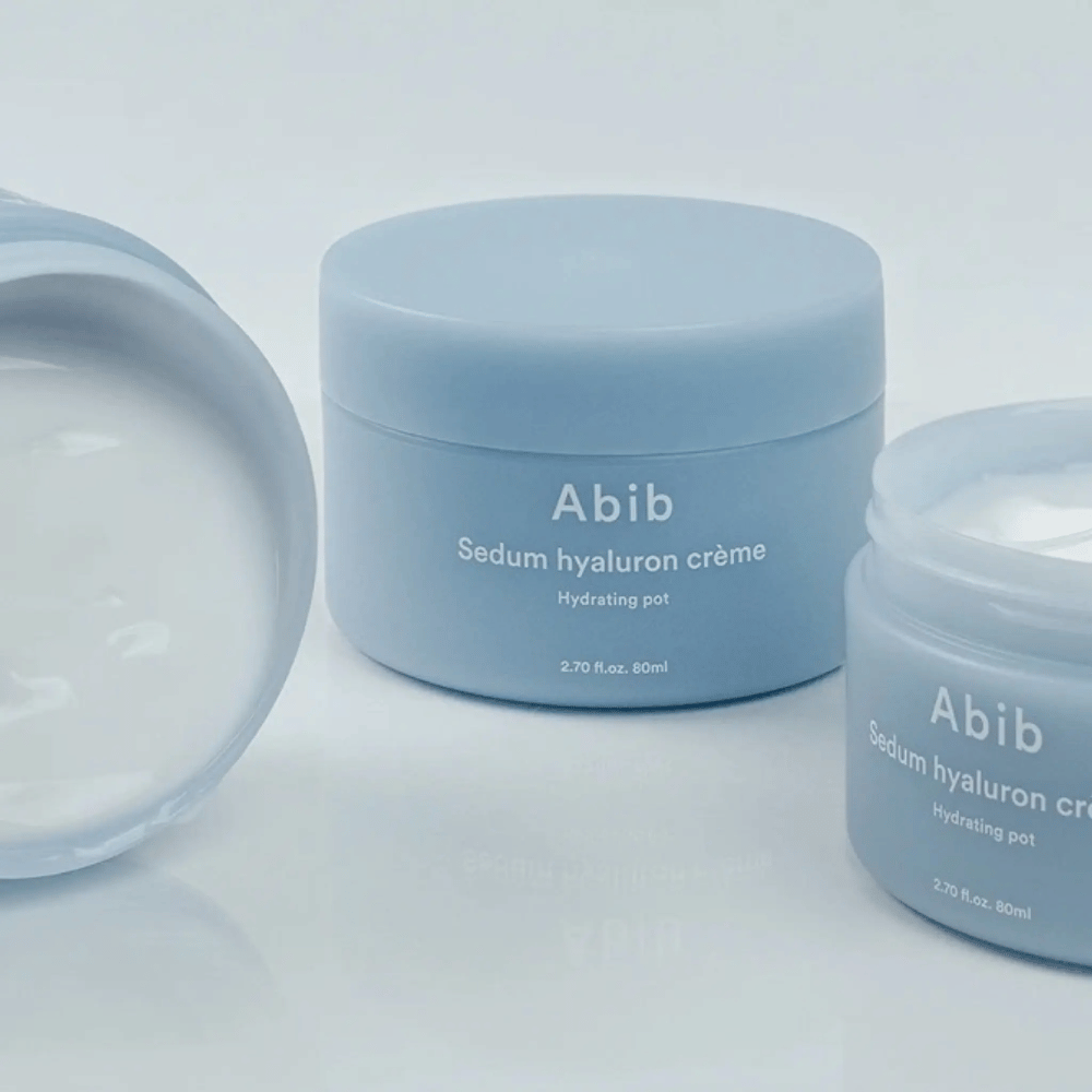 Kolme purkkia Abib Sedum Hyaluron Crème Hydrating Pot 80 ml vaaleansinisessä minimalistisessa designissa, joista yksi avoin purkki näyttää kermamaisen valkoisen koostumuksen.
