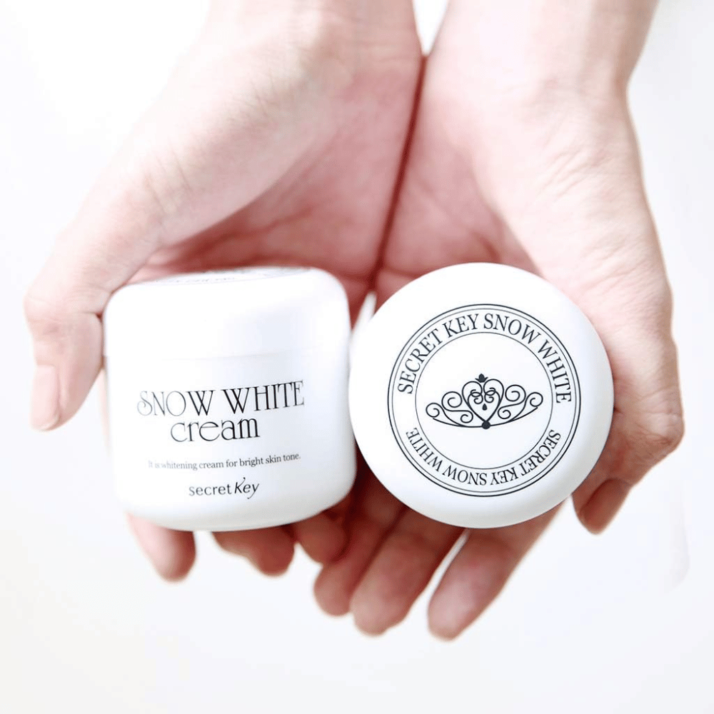 Kaksi purkkia Secret Key Snow White Cream pidetään käsissä, yksi näyttää kannen ja toinen etupuolen.