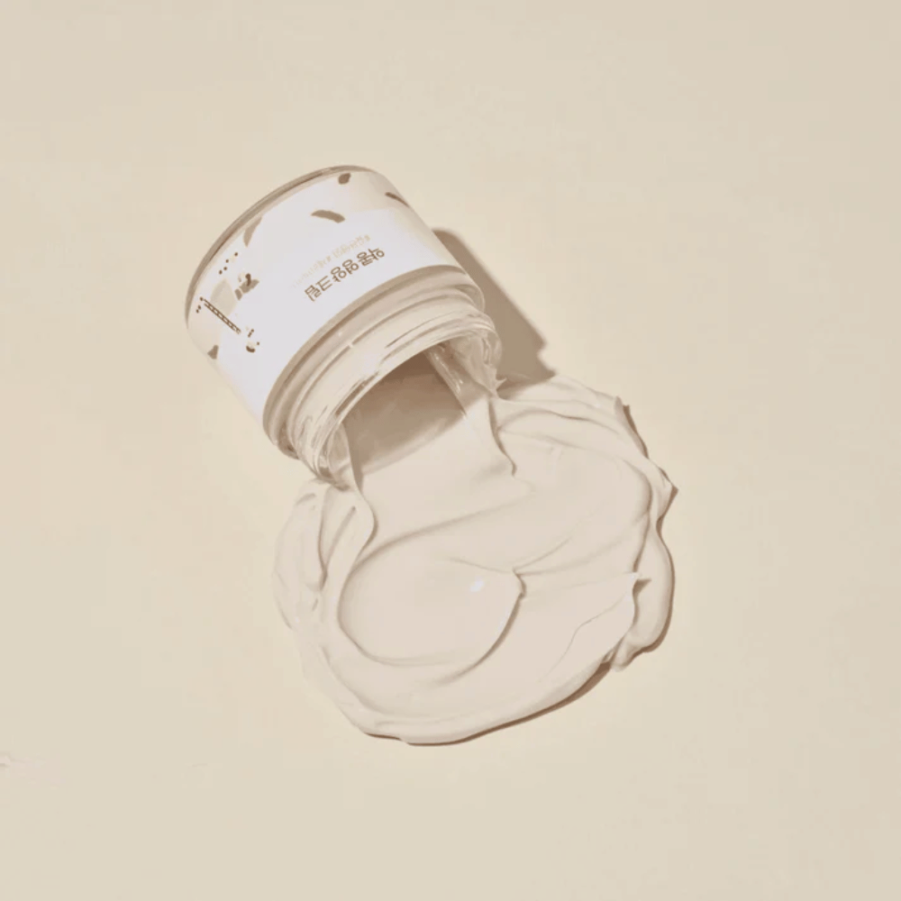 Mixsoon Soybean Nourishing Cream kaatui purkista beigelle taustalle. Voiteen täyteläinen koostumus osoittaa sen intensiiviset kosteuttavat ominaisuudet.