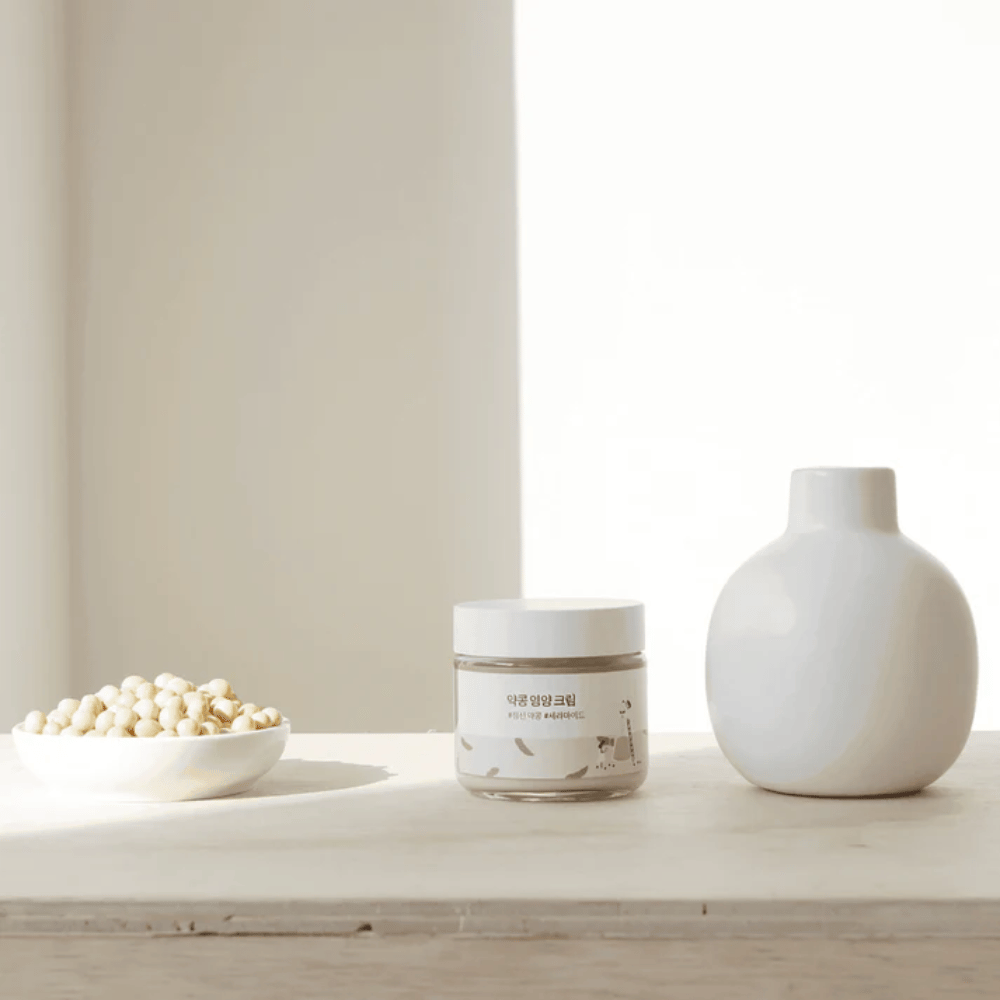 Mixsoon Soybean Nourishing Cream seisoo puupöydällä maljakon ja soijapapujen vieressä. Minimalistinen, kosteuttava voide luonnollisilla aineosilla.