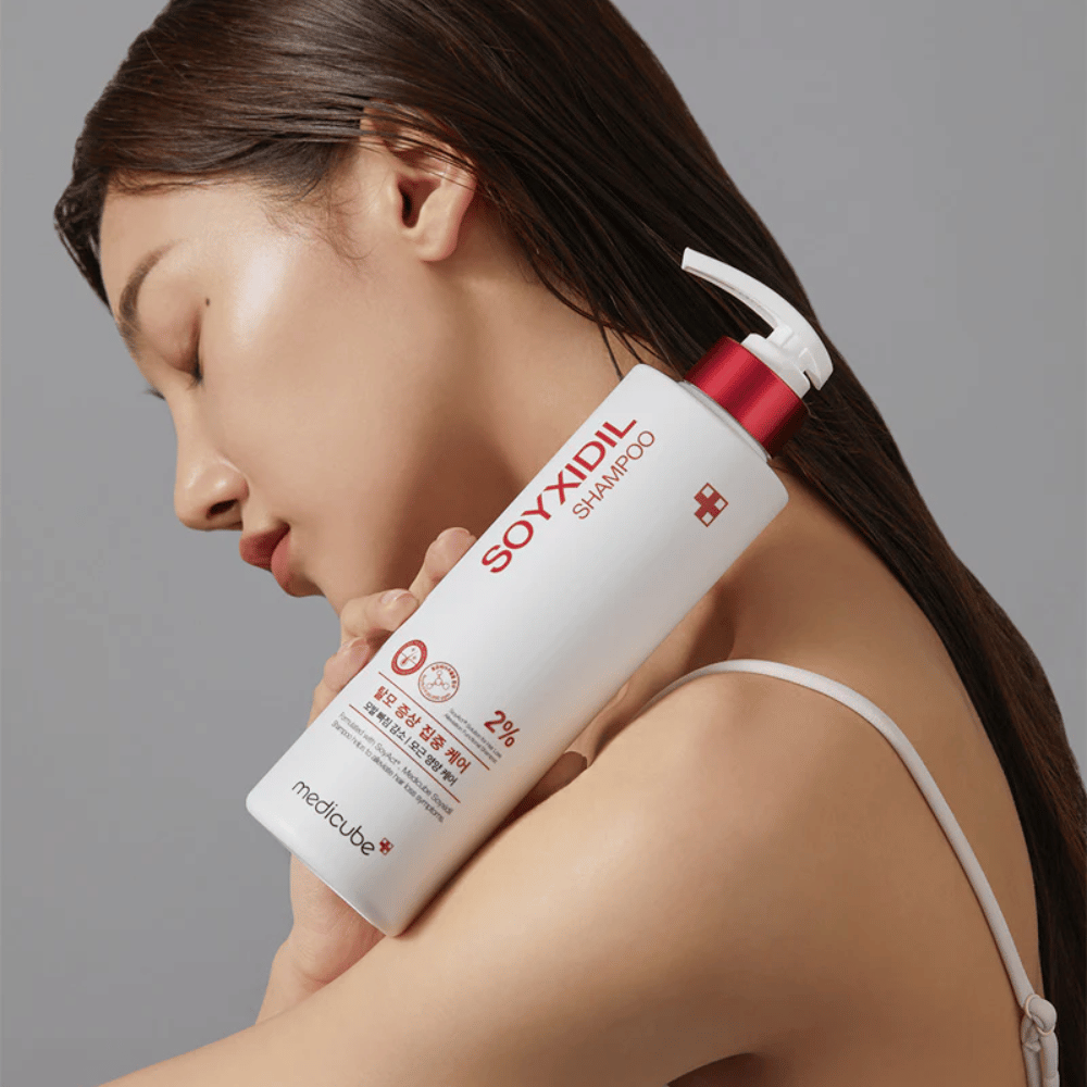 Nainen, jolla on pitkät hiukset, nojaa päätään pulloon Medicube Soyxidil Shampoo, joka vahvistaa hiuspohjaa ja ehkäisee hiustenlähtöä.
