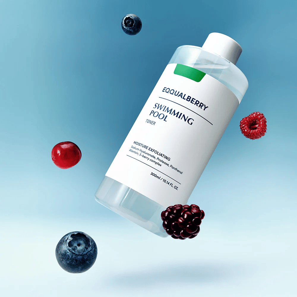 Equalberry Swimming Pool Toner tyylikkäässä pullossa leijumassa sinistä taustaa vasten, ympäröitynä tuoreilla marjoilla kuten mustikoilla, vadelmilla ja karhunvatukoilla.