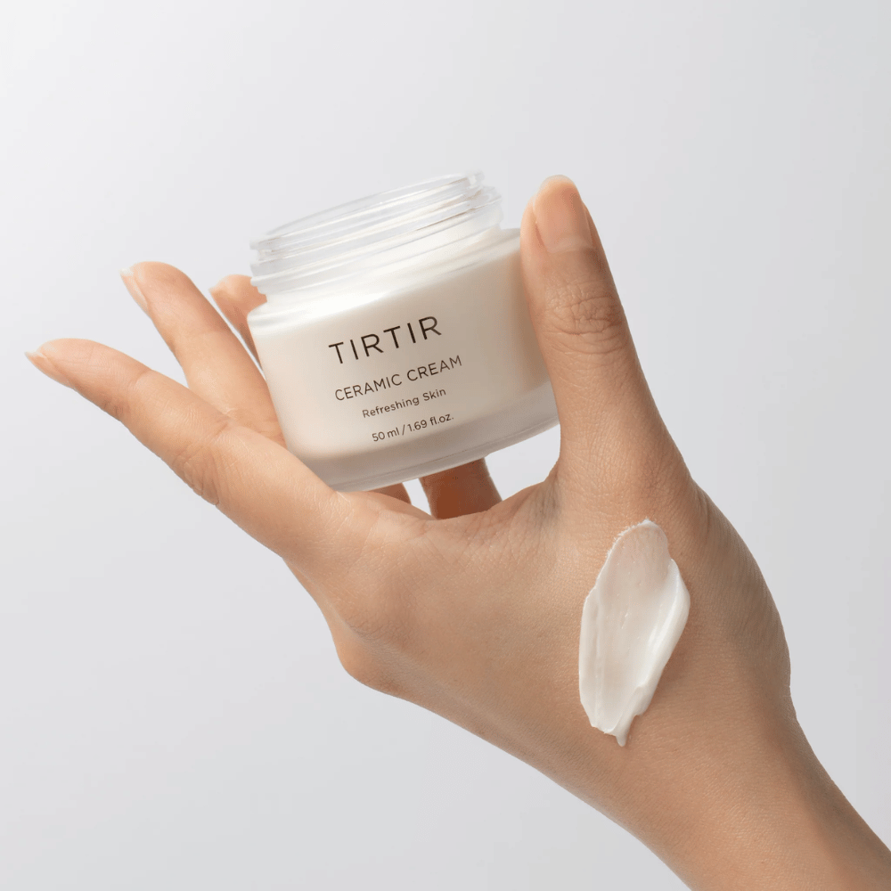 Käsi pitää purkkia, jossa on TIRTIR Ceramic Cream. Käden selkään on levitetty määrä voidetta. Voide näyttää olevan paksua ja kosteuttavaa. Pakkauksessa ilmoitetaan, että sisältö on tarkoitettu "Refreshing Skin" -tuotteelle ja määrä on 50 ml / 1.69 fl oz.